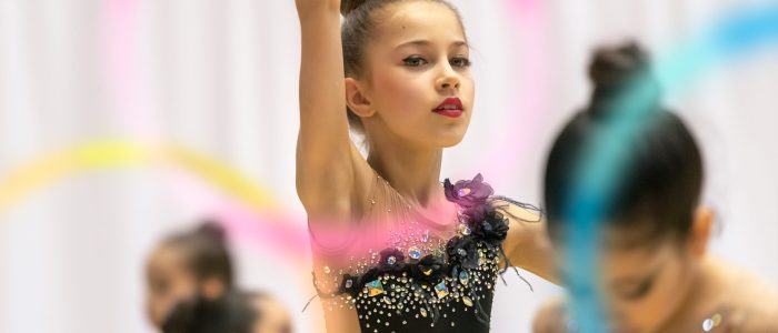 Portrait of a little pretty girl trying to win the rhythmic gymnastics championship, dancing with a hoop and wearing beautiful leotard embroidered with rhinestones